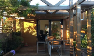 Terrasse extérieure en bois avec pergola et beaucoup de végétation.